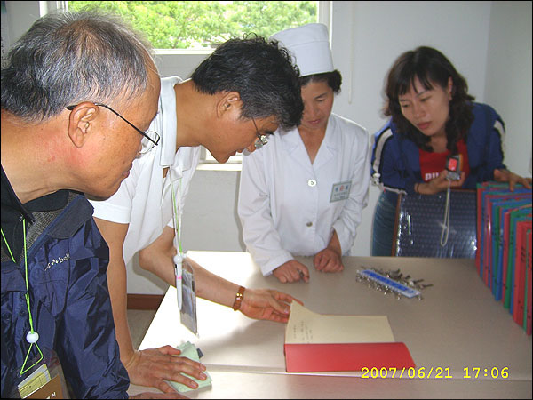 환자 병력카드...병력을 펜으로 기록한 노트를 보는 필자 일행과 병원장. 오른쪽 노트들이 병력카드철이다.