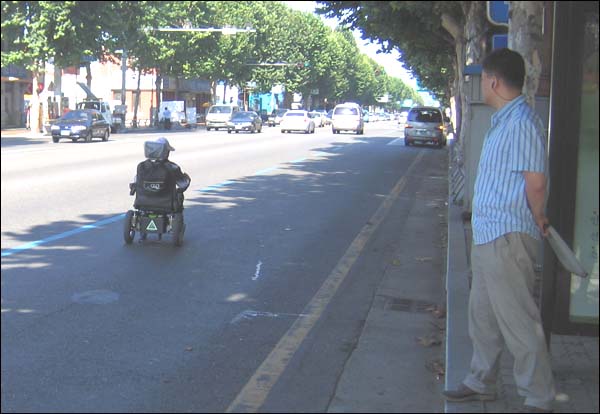 전동 휠체어를 탄 사람이 도로 한가운데를 지나고 있다.