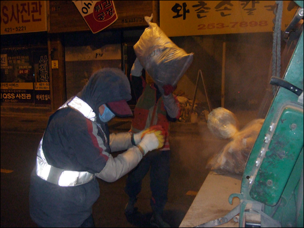 수거차량 뒤편 압착기에 쓰레기를 싣고 있는 환경미화원들. 연탄재가 많이 날려 마스크를 꼭 쓰고 일해야 한다 / 사진. 평화뉴스 박광일 기자