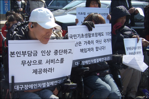 기자회견에 참석한 장애인들이 들고 있는 피켓. "본인부담금 인상 중단하고 무상으로 서비스를 제공하라", "국민기초생활보장제도 10년 가난은 가족이 아닌 국가가 책임져야 합니다"라고 적혀있다 / 사진. 평화뉴스 박광일 기자