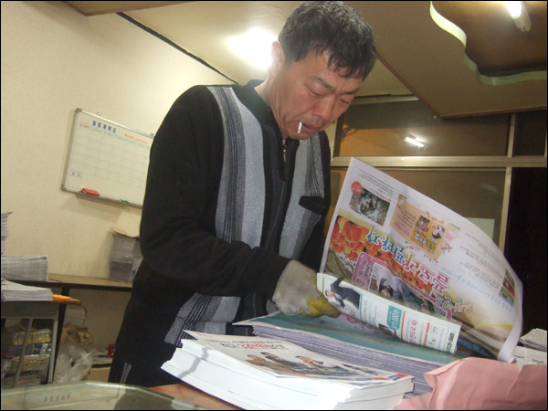 신문유통원 신암센터 김영식(54) 지국장이 신문 사이에 전단지를 끼워넣는 작업을 하고 있다 (2011.03.24) / 사진. 평화뉴스 박광일 기자