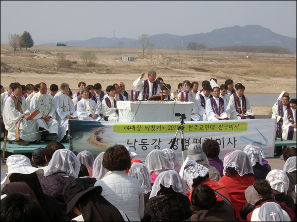 미사 강론을 하고 있는 대구대교구 허연구 원로사제와 공동 집전한 사제단 뒤로 황량한 낙동강변의 모습이 펼쳐져 있다 / 사진. 평화뉴스 박광일 기자