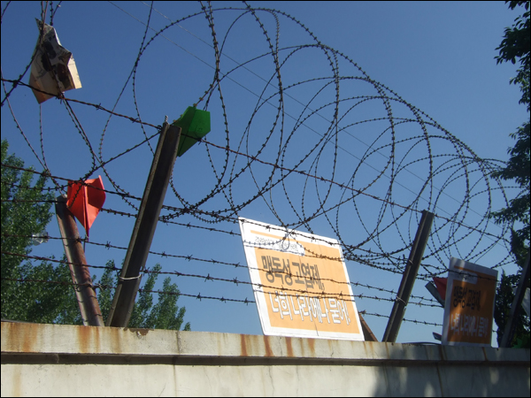 미군기자 담장 철조망에 결의대회 참가자들이 날려보낸 종이비행기와 '맹독성 고엽제, 너희나라에 묻어'라는 문구가 적힌 피켓이 걸려있다 / 사진. 평화뉴스 박광일 기자