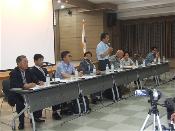 주민설명회를 열고 캠프캐럴 미군기지 헬기장에서 진행한 중간 조사결과를 발표하고 있는 한미공동조사단. 한국측 조사단장인 옥곤 부경대 교수가 자리에 서서 설명을 하고 있으며, 그 오른쪽에는 미국측 조사단장인 버치마이어 주한미군사령부 공병참모부장이 앉아있다 (2011.07.08) / 사진. 평화뉴스 박광일 기자