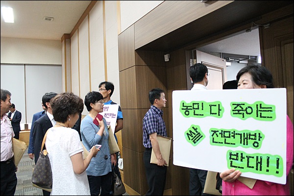 설명회 무산으로 대구상공회의소를 빠져나가는 공무원들 옆으로 한 농민이 "농민 다 죽이는 쌀 전면개방 반대" 피켓을 들고 있다(2014.6.24) / 사진. 평화뉴스 김영화 기자