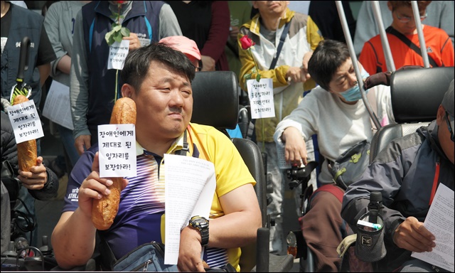 빵을 들고 '최저임금 준수'를 촉구하는 한 장애인(2018.4.30) / 사진.평화뉴스 김지연 기자