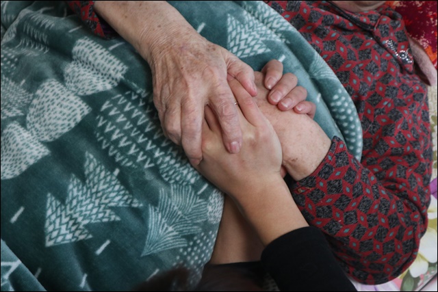 ▲건강 악화로 침대에 누워 설 인사를 온 이들의 손을 잡은 할머니(2019.1.30) / 사진.평화뉴스 김영화 기자