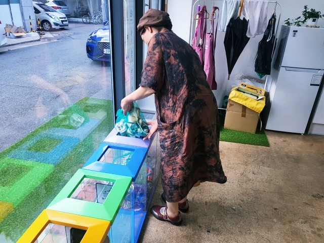 센터 인근에서 식당을 운영하는 이금희(65)씨가 요구르트병을 수거함에 담는 모습(2023.7.26) / 사진. 평화뉴스 정준민 기자