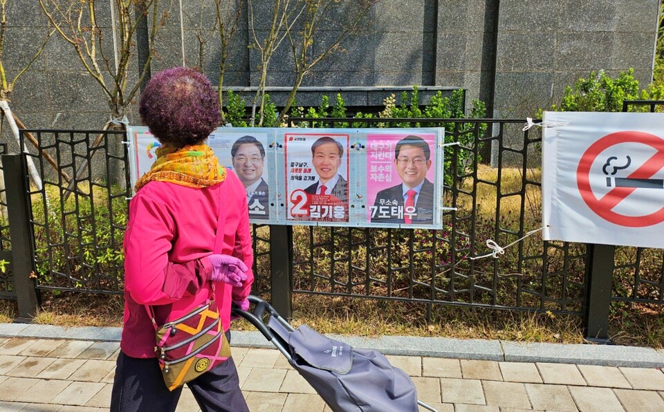 한 유권자가 대구 중구 남산4동 아파트단지 울타리에 붙은 선거 공보물을 보며 지나가고 있다. (2024.3.29) / 사진.평화뉴스 정준민 기자