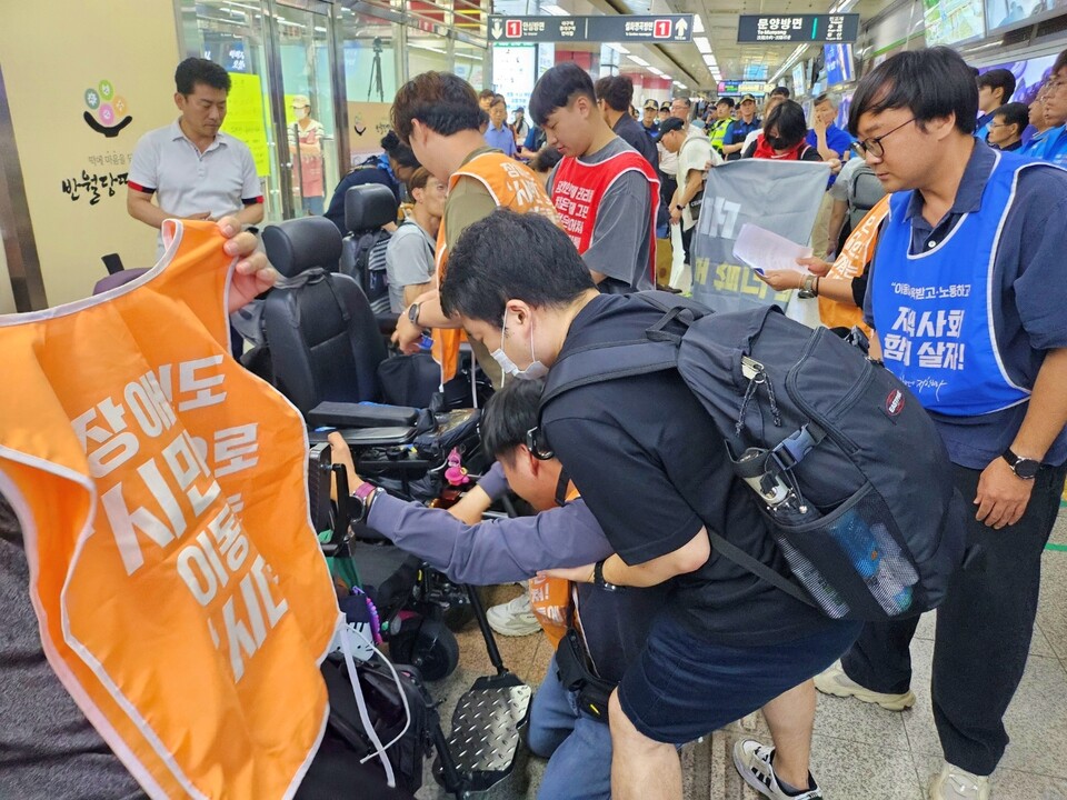 한 장애인이 반월당역 바닥에 눕기 위해 도움을 받으며 휠체어에서 내리고 있다.(2024.6.27) / 사진.평화뉴스 정준민 기자