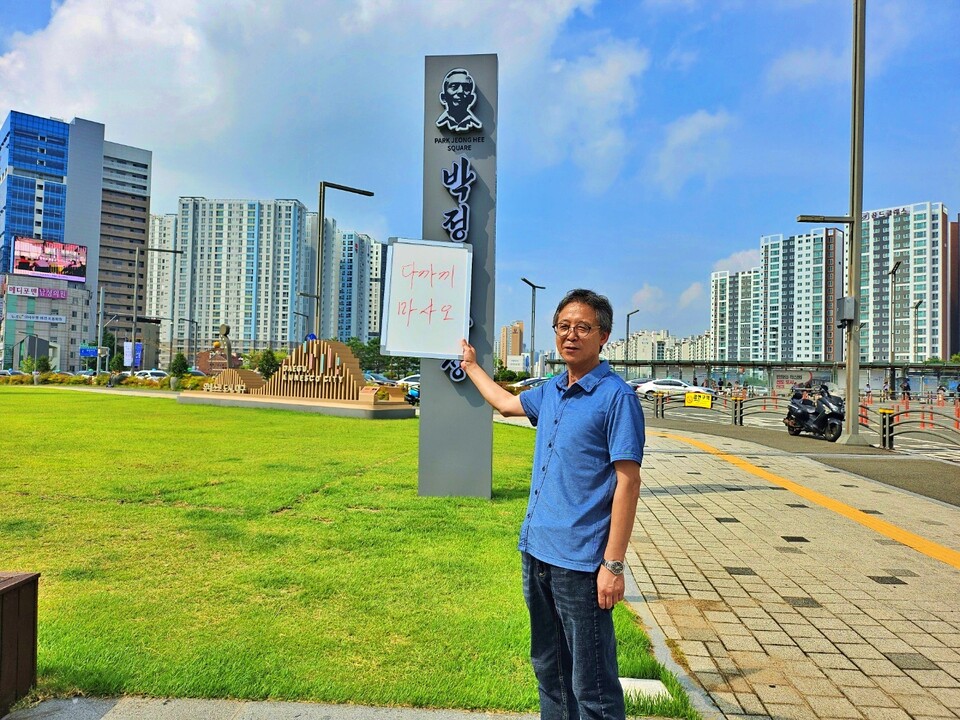 강금수 대구참여연대 사무처장이 동대구역 광장에 대구시가 설치한 '박정희 광장' 표지판 앞에서 박정희 기념사업을 비판하는 보드를 들고 서 있다.(2024.9.13) / 사진.평화뉴스 정준민 기자