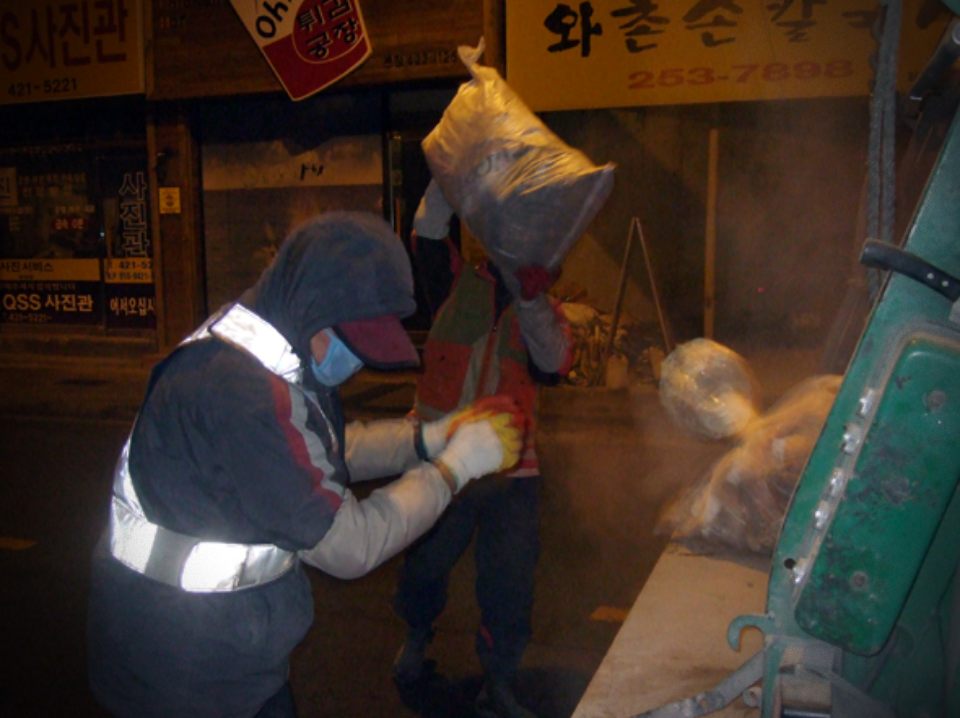 쓰레기 수거 차량 뒤편 압착기에 쓰레기를 싣는 환경미화원 노동자들(2011.1.18) / 사진.평화뉴스 기자 