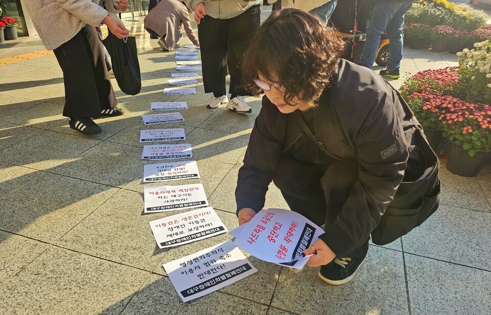 "행정편의주의식 이용자 범위 축소 반대한다" 대구장애인차별철폐연대 회원들이 대구시청 동인청사 바닥에 피켓을 붙이고 있다.(2024.11.13) / 사진.평화뉴스 정준민 기자