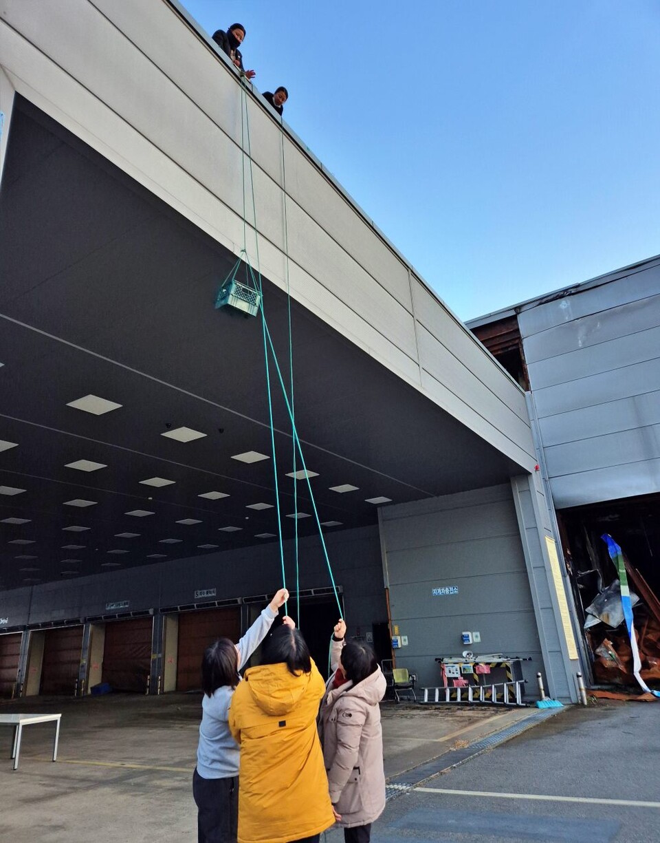 고공농성 중인 박정혜, 소현숙 두 여성 해고자들에게 깜짝 산타로 방문한 대경여연 회원들이 도르래를 이용해 음식을 올려보내고 있다.(2024.12.24) / 사진.대경여연