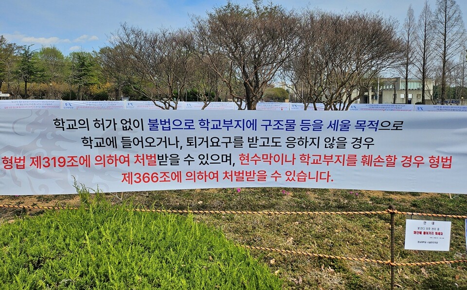 "학교 허가 없이 불법으로 학교 부지에 구조물 들을 세울 목적으로 학교에 들어오거나, 퇴거 요그를 받고도 응하지 않을 경우 형법에 의해 처벌받을 수 있다"는 내용의 경고 현수막
