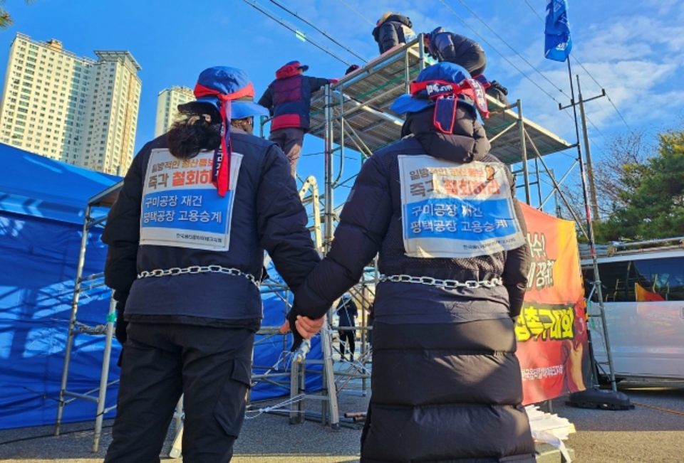 쇠사슬을 감은 경북 구미 한국옵티칼 해고노동자들이 망루 위 다른 해고자들을 보고 있다.(2024.2.16) / 사진.평화뉴스 정준민 기자