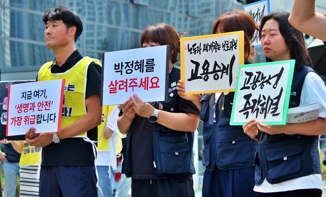 "박정혜를 살려주세요", "지금 여기 생명과 안전 가장 위급합니다", "고공농성 즉각 해결" 한국옵티칼 해고노동자들이 피켓을 들고 있다.(2025.7.26) / 사진.평화뉴스 정준민 기자