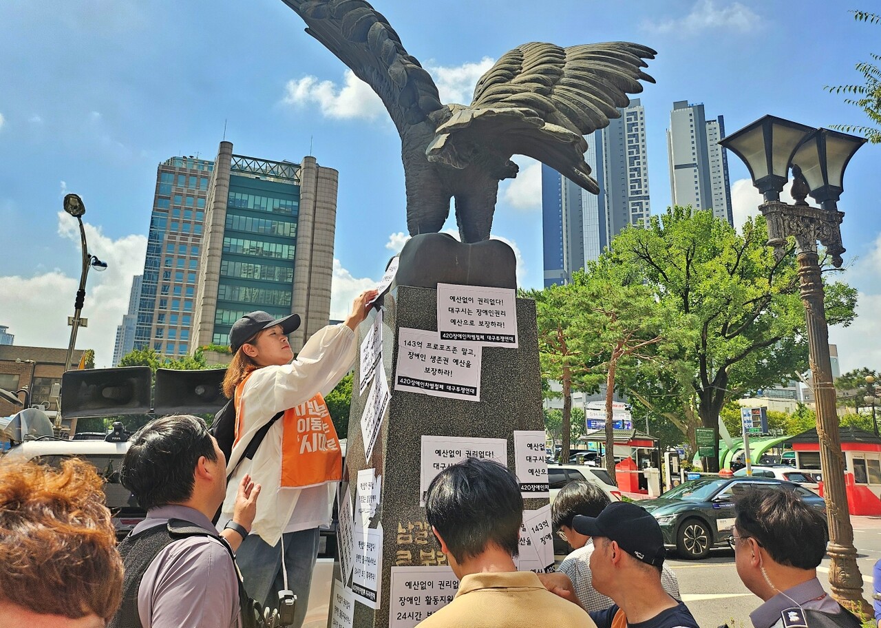 장애인단체 인사들이 대구시청 동인청사 앞 조형물에 "장애인권리 예산 보장" 스티커를 붙이고 있다.(2025.9.3) / 사진.평화뉴스 정준민 기자