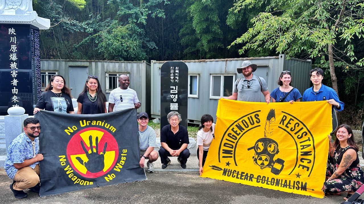 원폭 피해 2세인 고(故) 김형률씨의 비석 앞에서 '비핵평화' 깃발을 들고 사진을 찍는 이들(2025.8.6) / 사진.합천비핵평화대회