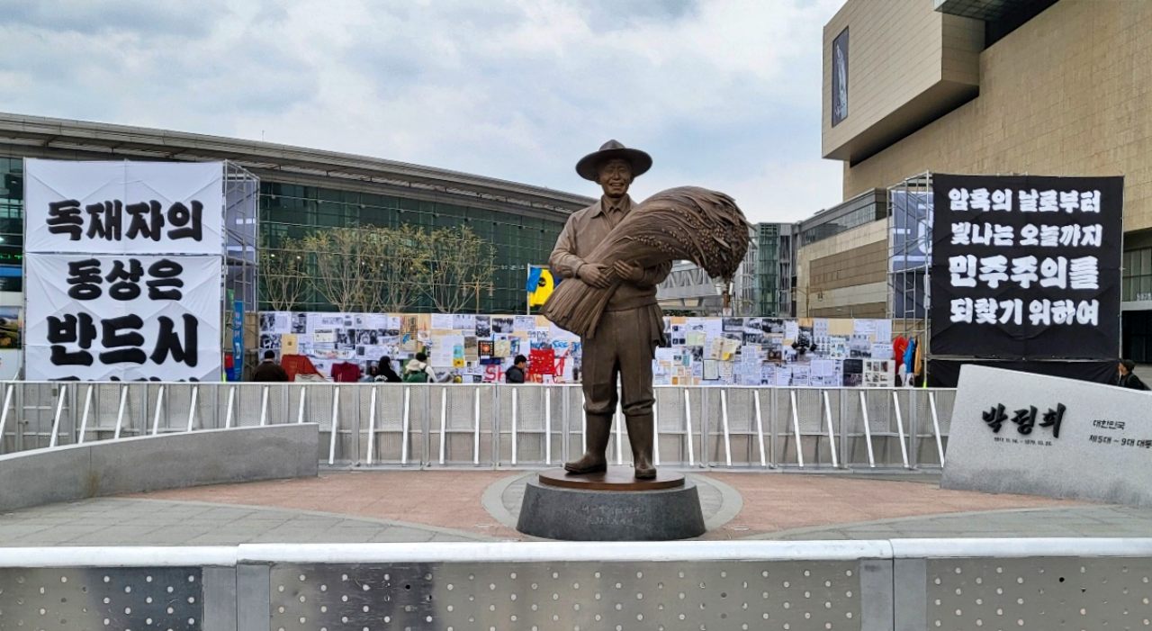 동대구역 광장에 선 박정희 동상...그 뒤로 시민단체가 설치한 "독재자의 동상은 반드시 무너진다 " 현수막이 보인다(2025.4.5) / 사진.평화뉴스 김영화 기자
